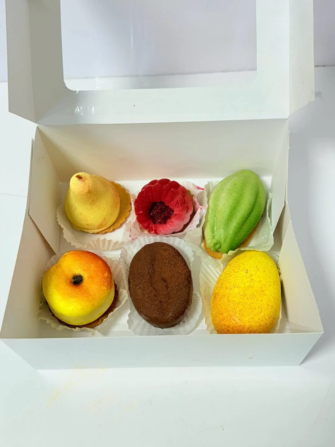 Cutie cu șase prăjituri în formă de fructe, fotografiată în atelier